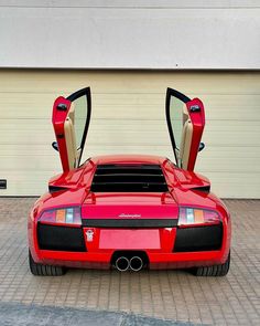 a red sports car parked in front of a garage door with its doors open to reveal the interior