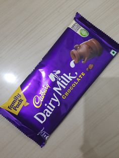 a bar of dairy milk sitting on top of a wooden table next to a cup