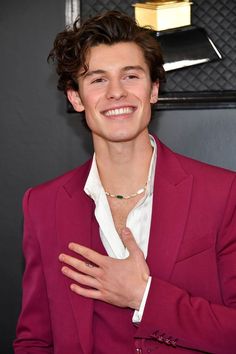 a young man in a red suit and white shirt with his hands on his chest