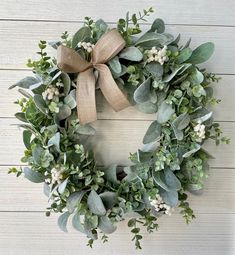 a wreath with greenery and burlap bow hanging on a white wooden wall