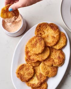 a white plate topped with fried food next to a cup of dipping sauce