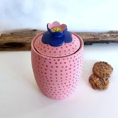 a cookie jar with a flower on top next to it and two cookies in the foreground