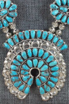 This Sleeping Beauty turquoise and sterling silver squash blossom, concho belt, earrings, pin/ pendant, bracelets, and rings set was made by Navajo silversmith Justina Wilson. The back is signed JW and stamped sterling.Squash BlossomLength: 26 1/2"Naja Height: 3"Naja Width: 2 3/4"Blossom Length: 2 1/8"Blossom Width: 1 1/8"Concho BeltBelt Length: up to 49"Belt Buckle Length: 3"Belt Buckle Width: 2"Concho Length: 2 1/2"Concho Width: 1 3/4"EarringsLength: 1 5/8"Width: 1 1/8"Pin/ PendantLength: 1 3/ Blue Western Style Jewelry With Inlay, Traditional Silver Turquoise Concho Necklace, Traditional Silver Turquoise Necklace With Concho, Traditional Blue Concho Jewelry, Blue Southwestern Jewelry With Concho, Sterling Silver Turquoise Concho Jewelry, Southwestern Blue Concho Jewelry, Western Style Oval Concho Jewelry, Artisan Oval Concho Jewelry