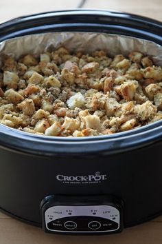 a crock pot filled with stuffing sitting on top of a wooden table