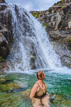 a woman sitting in the water next to a waterfall