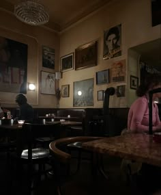 two people sitting at tables in a dimly lit room with posters on the wall behind them