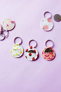 four different keychains with designs on them sitting next to each other in front of a purple background