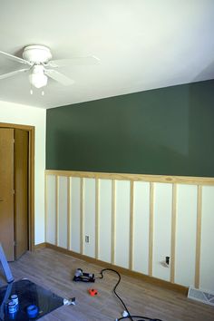 an empty room with green walls and wood paneling on the wall, including a ceiling fan