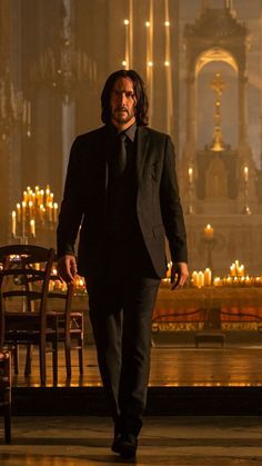 a man in a suit walking down a hall with candles on the wall behind him