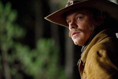 a man wearing a hat and coat in the dark with trees in the back ground