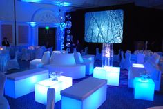 a room filled with lots of white couches and tables covered in blue lights at night