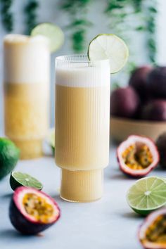 a glass filled with liquid next to sliced fruit and limes on a counter top