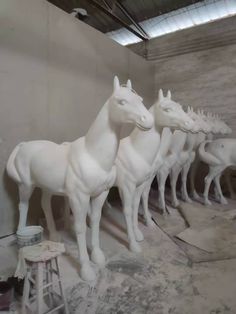 a group of white horses standing next to each other on top of a cement floor