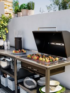 an outdoor bbq grill with plates and bowls on the table next to potted plants