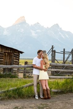 a man and woman standing next to each other in front of a fence with mountains behind them