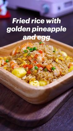 fried rice with golden pineapple and egg in a wooden bowl on a table next to a computer