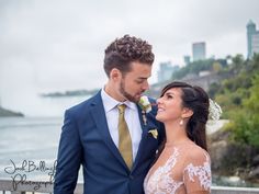 a bride and groom standing next to each other in front of the water with a city skyline behind them