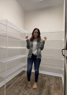 a woman standing in front of a closet full of white shelvings and shelves