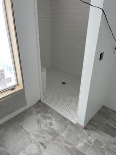 an empty bathroom with tile flooring and a shower stall next to a large window