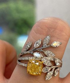 a woman's hand holding a yellow diamond ring with leaves on the top and bottom