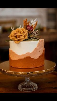 a white and orange cake with flowers on top sitting on a gold plated platter