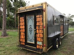 a black and gold colored bus parked in the grass near some trees with its door open