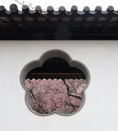 a window with a view of cherry blossoms in the background and behind it is a white wall