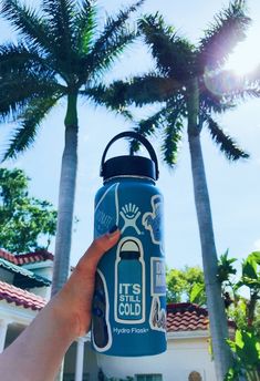 a person holding up a water bottle in front of palm trees with the words it's cold on it