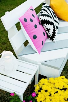 a white bench with some pillows on top of it next to flowers and a candle