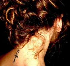 the back of a woman's neck with a cross tattoo on her left shoulder