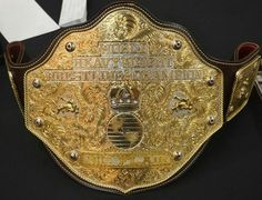 a gold wrestling belt is displayed on a black surface