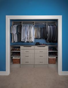 an open closet with clothes and baskets on the bottom shelf, next to a blue wall