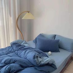 an unmade bed with blue sheets and pillows in a bedroom next to a window