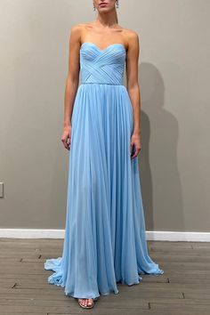 a woman in a blue dress standing on a wooden floor next to a gray wall