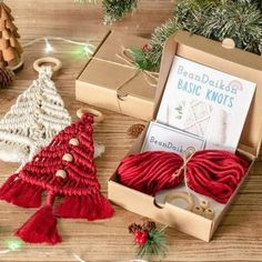 two knitted christmas tree ornaments in a box on a wooden table next to other crafting supplies