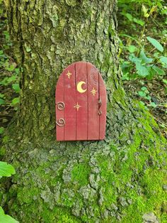 a red fairy door on the side of a tree in the woods with moss growing around it