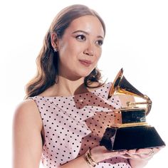 a woman holding an award in her hand and wearing a polka dot dress, standing against a white background