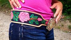 a woman wearing a pink shirt and blue jeans holding onto a belt with flowers on it