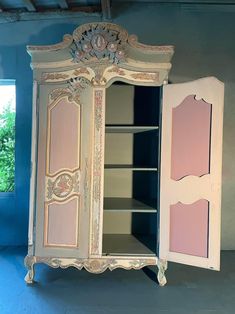 an old white cabinet with pink paint on the door and shelves in front of it