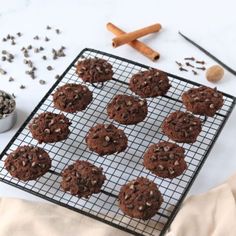 chocolate cookies cooling on a wire rack with cinnamon sticks and spices around them next to a cup of coffee