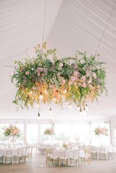 an overhead floral chandelier hangs from the ceiling in a tent with tables and chairs