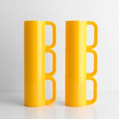 two yellow mugs sitting next to each other on a white counter top, one has the letter b in it's middle