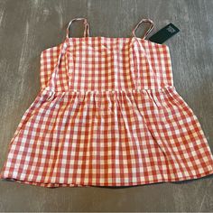 an orange and white checkered dress laying on the floor next to a pair of scissors