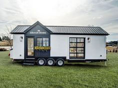 a tiny house on wheels is parked in the middle of a grassy field with windows