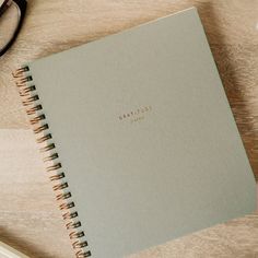 an open notebook sitting on top of a wooden table next to a pair of glasses