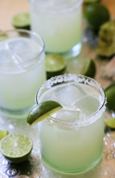 two margaritas are garnished with lime and sugar on the rim, surrounded by lime slices