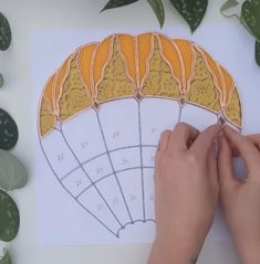 a person is drawing an orange and yellow fan on top of a sheet of paper