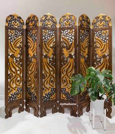 a room divider made out of wood with intricate carvings on it and a potted plant next to it