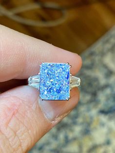 a person's hand holding a ring with blue and white glitter on it,