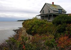 an old house sitting on top of a cliff next to the ocean with trees and bushes around it